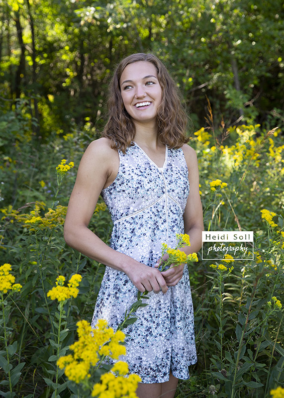 natural and fun high school senior girl in a woodsy field of yellow flowers during her senior picture session 